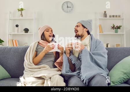 Junges Paar eingewickelt in warme Decken sitzen auf Couch und Niesen in Papiertaschentücher Stockfoto