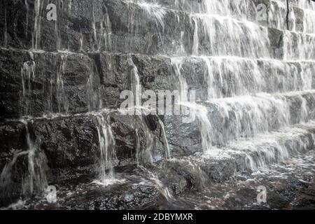 Vollformat-Langzeitbelichtung eines mehrstufigen Wasserfalls, Nahaufnahme zeigt Bewegung und Ablagerung von Wasser und rauer Steinheft. Stockfoto