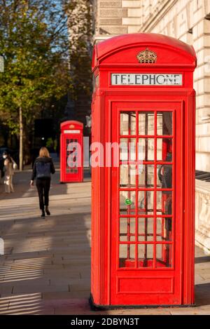 Ikonische rote Londoner Telefonzellen in Westminster, London, Großbritannien. Frau, die vorbeigeht. Rote Telefonbox. Heller sonniger Tag mit wenigen Menschen im Lockdown Stockfoto