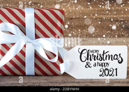 Ein Weihnachtsgeschenk mit Etikett mit Egnlish Kalligraphie Frohe Weihnachten und EIN glückliches 2021. Geschenkpapier mit SCHLEIFE und Schneeflocken Stockfoto