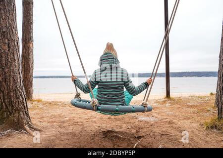 Nicht erkennbare Frau auf Swing Rückansicht. Fluss im Hintergrund, Natur und Ruhe. Selbstisolierung. Stockfoto