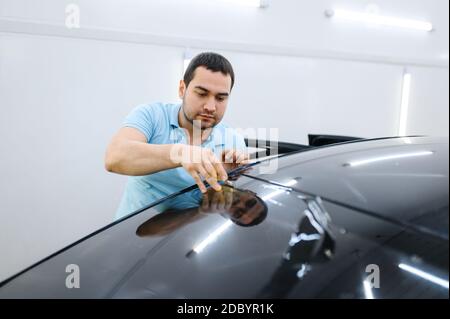 Männliche Wrapper schneidet Auto Färbung, Tuning-Service. Arbeiter, der Vinylfarbe auf das Fahrzeugfenster in der Garage aufgibt Stockfoto