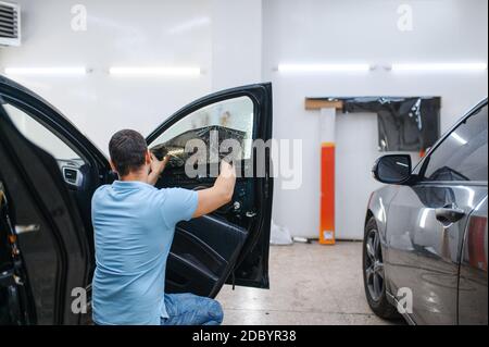 Männlicher Spezialist installiert benetzte Auto Färbung, Tuning-Service. Mechaniker, der Vinylfarbe auf das Fahrzeugfenster in der Garage aufgibt Stockfoto