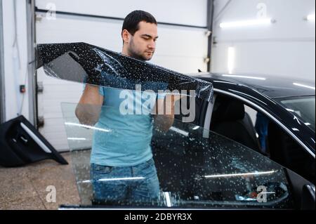 Männlicher Spezialist installiert benetzte Auto Färbung, Tuning-Service. Mechaniker, der Vinylfarbe auf Fahrzeugfenster in der Garage aufsetzt, getöntes Automobilglas Stockfoto