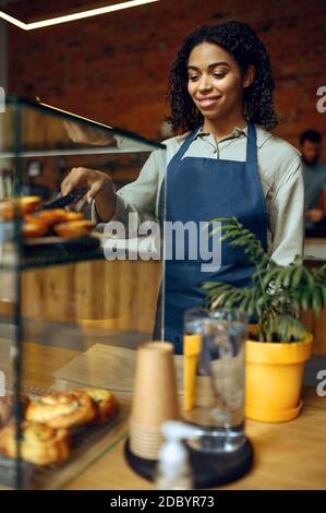 Weibliche Barista auf der Schürze hält Teller mit Croissant im Café. Frau, die in der Cafeteria Süßigkeiten auswählte, Kellner an der Theke in der Bar Stockfoto