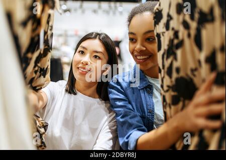 Zwei Mädchen Wahl Kleider im Bekleidungsgeschäft. Frauen, die in der Modeboutique einkaufen, Shopaholics, Shopper, die Kleidung auf Kleiderbügeln suchen Stockfoto