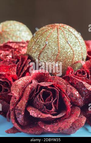 Eine rote Rose aus Stoff mit Glitzern und Glitzer mit dekorativen Weihnachtskugeln im Hintergrund. Traditionelle Feiertage. Stockfoto