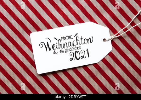 Label mit deutscher Kalligraphie Frohe Weihnachten und ein glückliches 2021 bedeutet Frohe Weihnachten und EIN glückliches 2021. Rotes Geschenkpapier Als Hintergrund Stockfoto