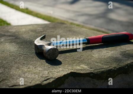 Ein Hammer mit einem roten und schwarzen Griff auf einem Kopfsteinpflaster Säule auf einer Suburban Street Stockfoto