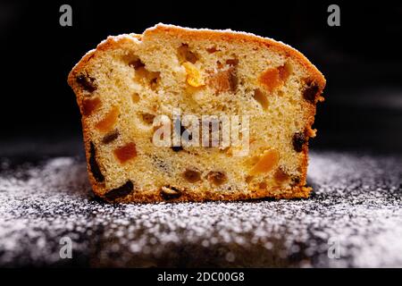 Süßer Cupcake in Form von Brot. Cupcake mit Rosinen, getrockneten Aprikosen, Pflaumen. Brot - Cupcake auf einem Holzbrett auf schwarzem Hintergrund, bestreut w Stockfoto