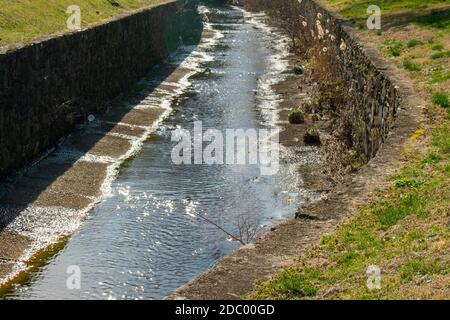 Ein von Menschen gemachter Kanal mit Kopfsteinpflasterwänden für Entwässerung und Überlauf Stockfoto