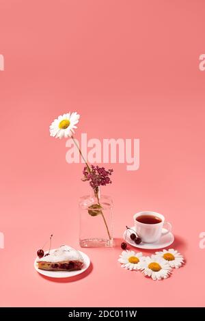 Stück Kirschkuchen auf einem Teller mit Tee in einem weißen Becher. Rosa Hintergrund Stockfoto