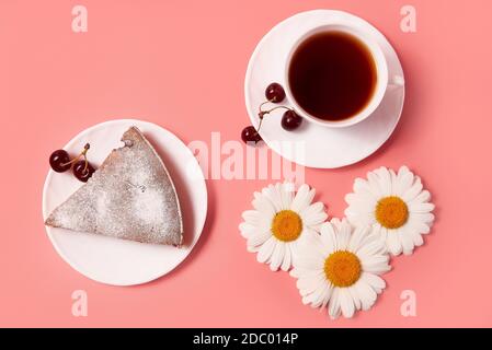 Stück Kirschkuchen auf einem Teller mit Tee in einem weißen Becher. Rosa Hintergrund Stockfoto