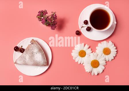 Stück Kirschkuchen auf einem Teller mit Tee in einem weißen Becher. Rosa Hintergrund Stockfoto