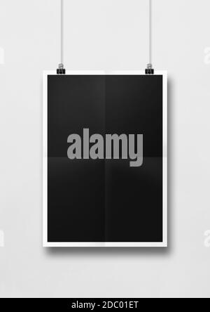 Schwarzes gefaltetes Poster, das an einer weißen Wand mit Clips hängt. Leere Mockup-Vorlage Stockfoto