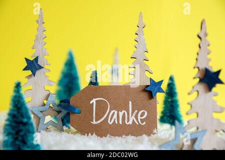 Label mit deutschem Text Danke bedeutet Danke. Weihnachtsbäume Mit Sternendekor Und Ornament. Gelber Hintergrund Mit Schnee Stockfoto