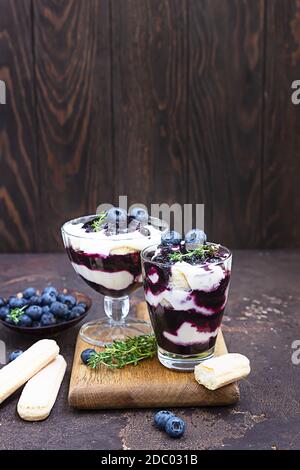 Dessert aus Mascarpone oder Ricotta-Käse, Heidelbeeren und Keks im Glas auf dunklem Hintergrund. Kein gebackener Käsekuchen oder Tiramisu. Stockfoto