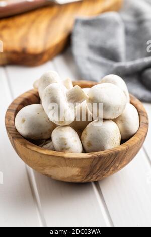Frische weiße Champignon-Pilze in Holzschüssel auf weißem Tisch. Stockfoto