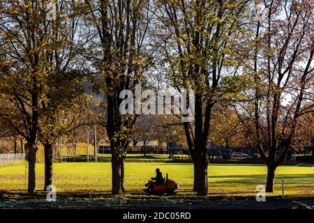 Freiburg, Deutschland. November 2020. Ein Mann fährt auf einem Sportplatz an der Albert-Ludwigs-Universität Freiburg einen Aufsitzmäher zwischen den Bäumen. Für heute prognostizieren Meteorologen in Freiburg Höchstwerte von bis zu 15 Grad Celsius und strahlenden Sonnenschein. Quelle: Philipp von Ditfurth/dpa/Alamy Live News Stockfoto