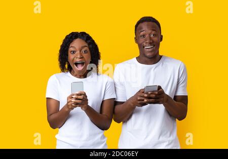 Erstaunt afroamerikanischen Mann und Frau halten Smartphones Stockfoto