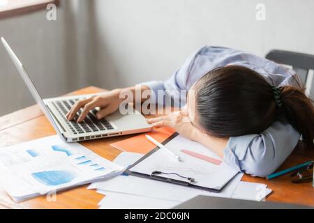 Asiatische Geschäftsfrauen fühlen sich schläfrig, nachdem sie lange Zeit am Schreibtisch vor dem Laptop gearbeitet haben. Geschäfts- und Finanzkonzept. Stockfoto