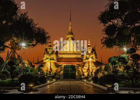 Ordination Hall neben einem buddhistischen Tempel Wat Arun in Bangkok.Thailand Wahrzeichen.Bunte Porzellanstatuen. Tempelwächter Figuren. Nächtliche Lichter der Stadt Stockfoto