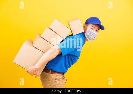 Asiatische junge Lieferung Arbeiter Mann in Uniform trägt Gesichtsmaske Schutz er hat viele Job Heben Stapel schwer eine Menge von Kisten auf dem Rücken, unter Coronavirus Stockfoto
