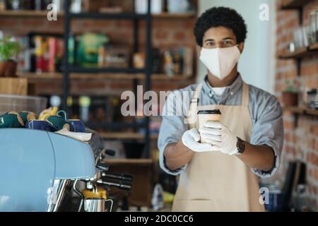 Kellner in medizinischer Schutzmaske serviert Kaffee im Restaurant während Coronavirus Pandemie und neue Normalität Stockfoto