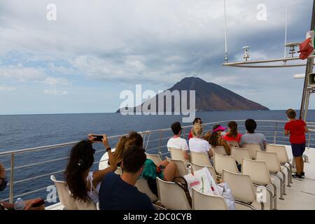 Sizilien, Italien. Touristen auf dem Deck eines Sightseeing-Bootes beobachten und fotografieren eine Rauchwolke, die vom aktiven Vulkan Stromboli aufsteigt. Stockfoto