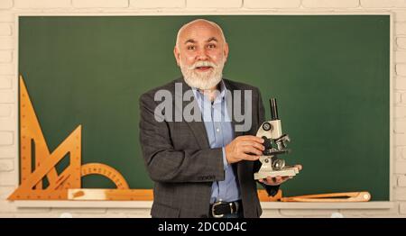 Formel. Chemie in der Schule. Wissenschaft Experimente mit Mikroskop im Labor. Biologie Schule Laborausrüstung. Mann im Klassenzimmer mit mathematischen Werkzeugen an der Tafel. Senior Lehrer verwenden Mikroskop. Stockfoto