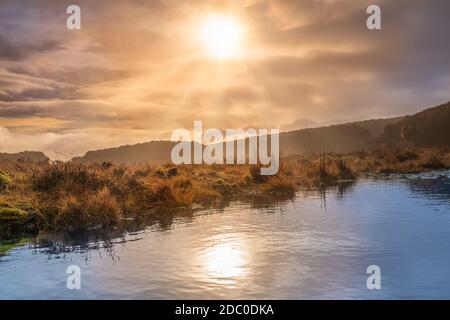 Nebel, Nebel und dramatischer Himmel über einem Sumpf oder Moor mit Sonne, die in einem See reflektiert. Dramatische Landschaft der Wicklow Berge, Irland Stockfoto