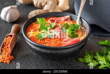 Schüssel mit Linsentomate und Kokosnusssuppe mit geschnittenem Schinken Stockfoto