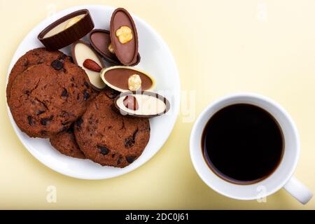 Schokolade, eine Tasse Kaffee und Kekse mit Schokoladenstückchen auf gelbem Hintergrund. Blick von oben. Stockfoto