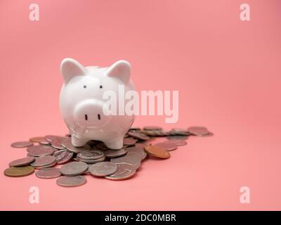 Weißes Sparschwein auf einem Stapel von Münzen auf einem rosa Hintergrund platziert. Sparkonzept. Stockfoto