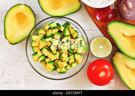 Avocado Hälften, Limetten Tomaten und Zwiebeln - grundlegende Guacamole Zutaten auf weißem Arbeitsbrett, Blick von oben. Stockfoto