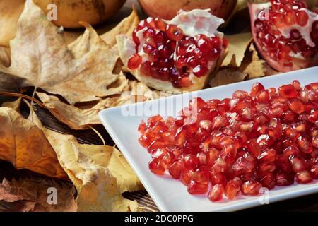 Nahaufnahme der roten Samen der Granatapfel-Frucht auf einem Teller bereit, zu essen und ein Split Granatapfel im Hintergrund. Hintergrund der trocken gefallenen lea Stockfoto