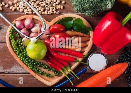 Weltessen-Tag, Draufsicht auf verschiedene frische Bio-Obst und Gemüse in Herzplatte und Arzt Stethoskop mit Kopierer Platz, Studio auf Holzregale aufgenommen Stockfoto