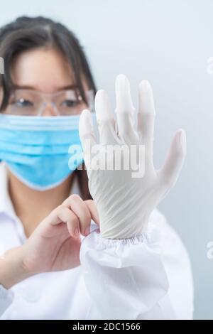 Nahaufnahme Wissenschaftler Hände Einlegen von Nitrilhandschuhen in Laborkittel Tragen von Nitrilhandschuhen, Experimentieren im Labor Stockfoto