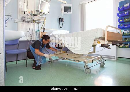 Ein Krankenhausreiniger wischt den Rahmen eines Bettes in einer modernen britischen Krankenstation ab. Stockfoto