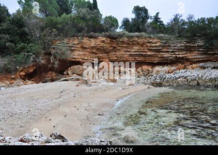 Abstrakte rote Klippe am kroatischen Strand, Holz aus der Adria. Strand Hintergrund. Abstrakt verwitterte Felsen am Sandstrand. Stockfoto