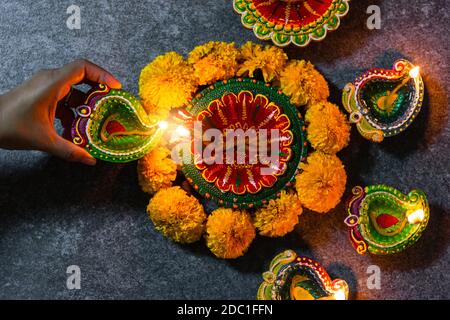 Nahaufnahme Frau Hand angezündet Ton Licht Feuer auf Diya oder Öllampe Studio auf schwarzem Holzhintergrund erschossen, Dekoration des Hinduismus rangoli, Happy Celebr Stockfoto