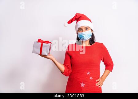Coronavirus weihnachtskonzept. Glückliche Frau hält Kisten mit Geschenken mit Gesichtsmaske, weihnachtsmann Kostüm lächelnd auf weißem Hintergrund. weihnachten während CO Stockfoto