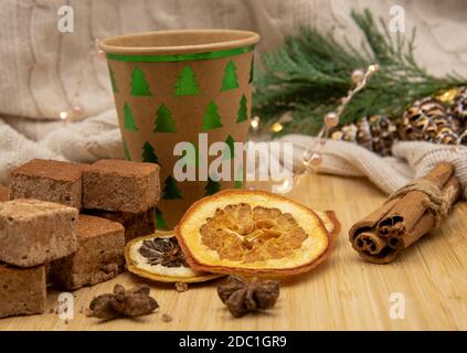 Einweg-Weihnachtsglas aus Pappe mit einem Getränk und verschiedenen Süßigkeiten Und aromatische Gewürze auf einem Holztablett mit einem verziert Fichtenzweig und ein Christm Stockfoto