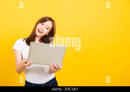 Asiatisches glückliches Porträt schöne niedliche junge Frau Teenager Lächeln stehend tragen T-Shirt halten Laptop Computer und freut sich, den Erfolg zu feiern, der zum Kamer schaut Stockfoto