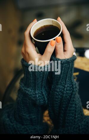 Der Mensch hält eine Tasse Kaffee mit zwei Händen in einem warmen herbstgrünen Pullover. Gemütliche Winteratmosphäre. Stockfoto