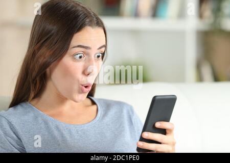 Überrascht Mädchen überprüft Smartphone sitzen auf einer Couch in Das Wohnzimmer zu Hause Stockfoto