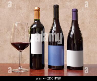 Drei Flaschen Wein und ein Glas Rotwein dagegen Strukturierter Hintergrund Stockfoto