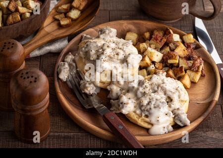 Kekse mit cremiger Wurstsoße und Bratkartoffeln auf einem Holzplatte Stockfoto