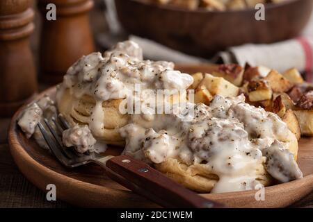 Nahaufnahme von Keksen mit cremiger Wurstsoße und Bratkartoffeln Auf einem Holzteller Stockfoto