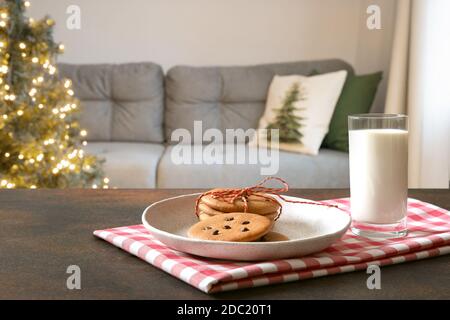 Kekse und Milch für den Weihnachtsmann auf dem Tisch im Wohnzimmer vor dem Weihnachtsbaum. Stockfoto